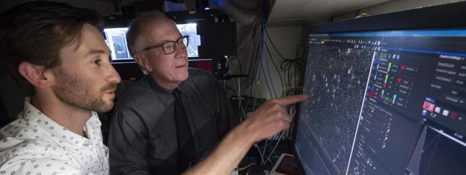Two men review an image from a high-powered microscope.