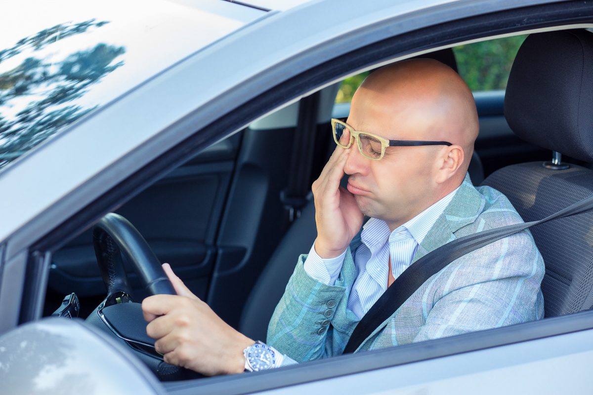 Sluggish man rubbing his eyes while driving due to daylight saving time