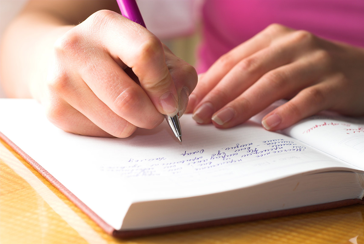 Person at a desk writing in a journal with a pen