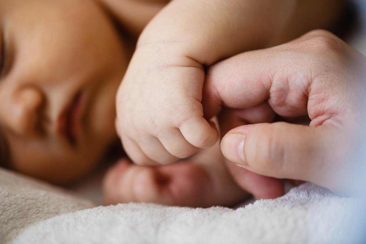 Newborn baby grasping an adult's finger