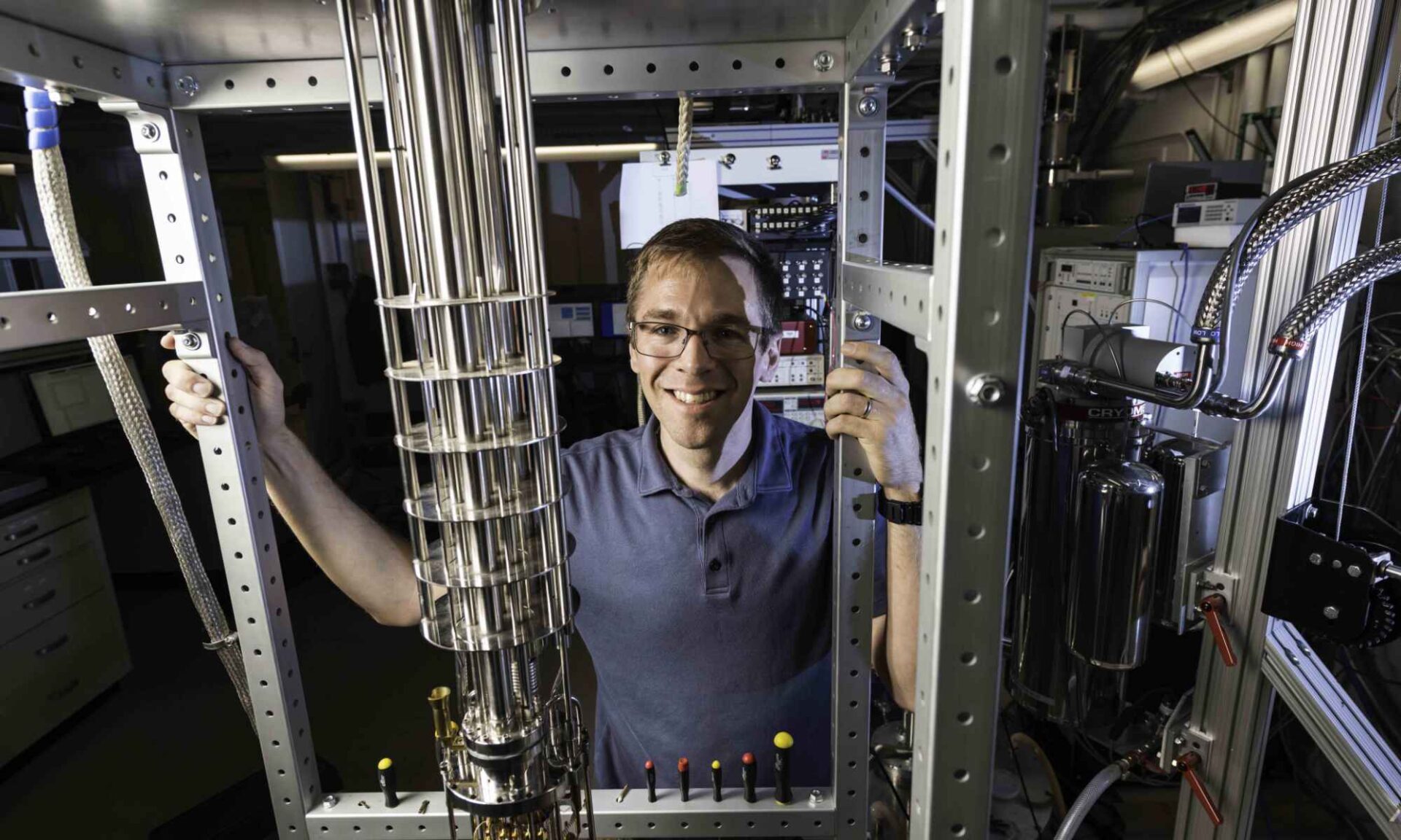 Physicist standing with a dilution refrigerator used to study quantum systems