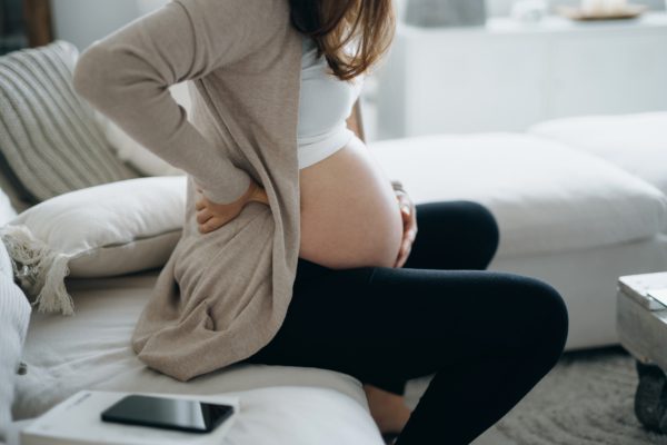 Pregnant woman holding stomach on couch with hyperemesis gravidarum