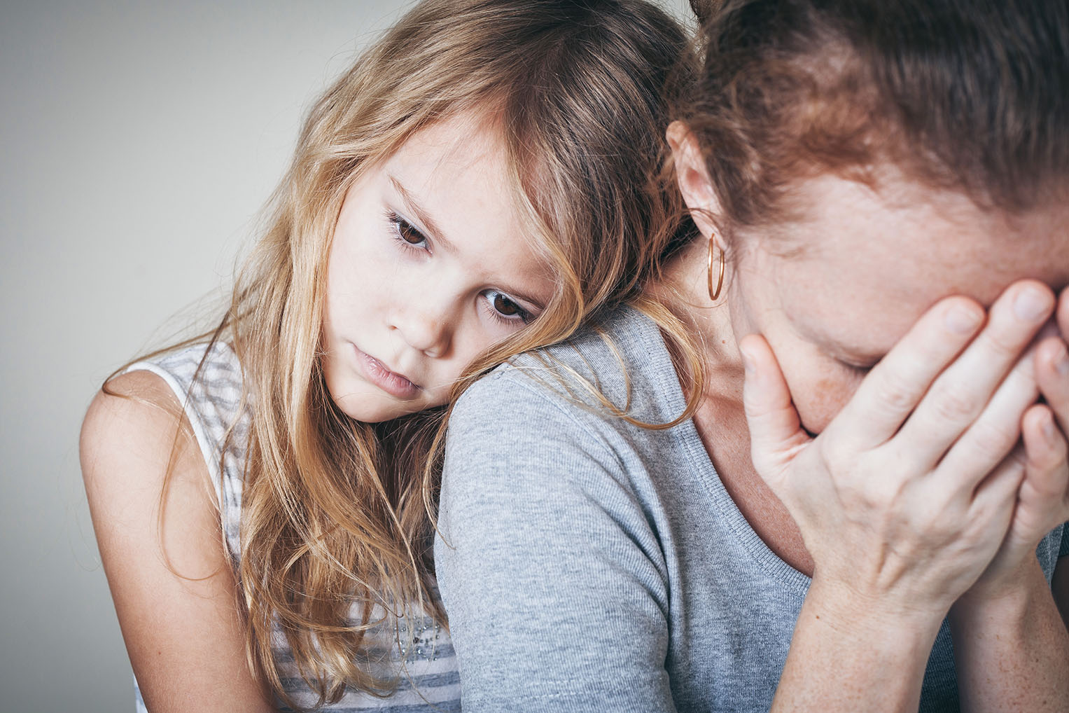 A child leans on a the shoulder of an upset adult.