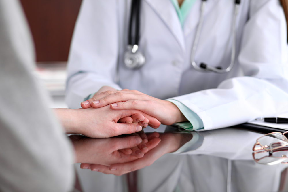 A doctor holds a patient's hand reassuringly.