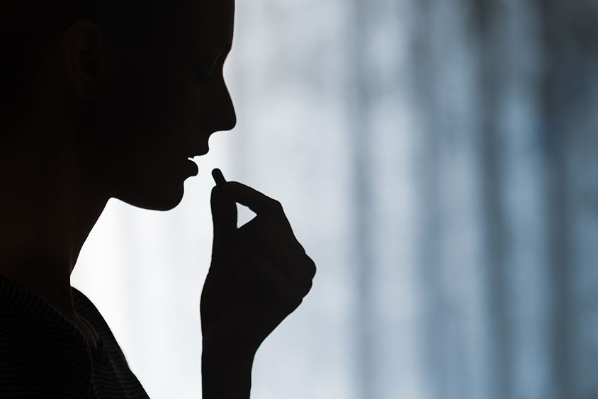 The silhouette of a person taking a pill.