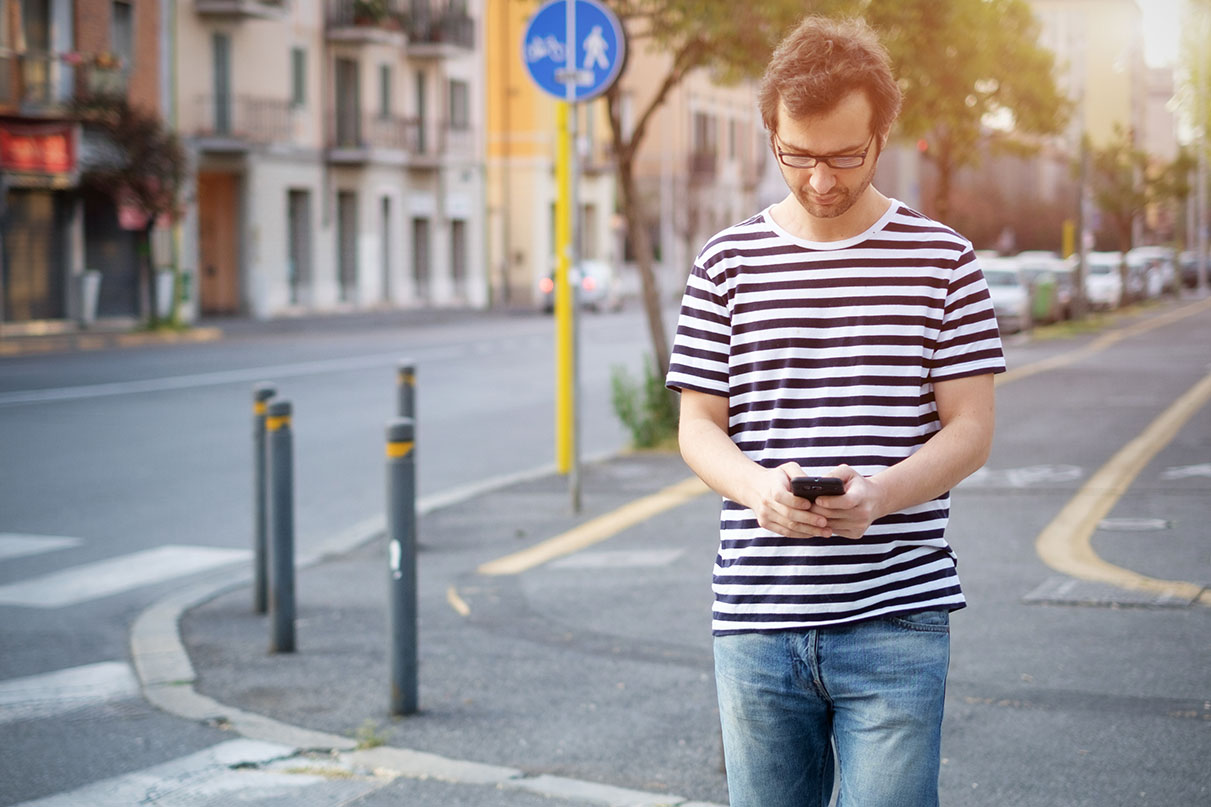 A person texts while walking across the street.