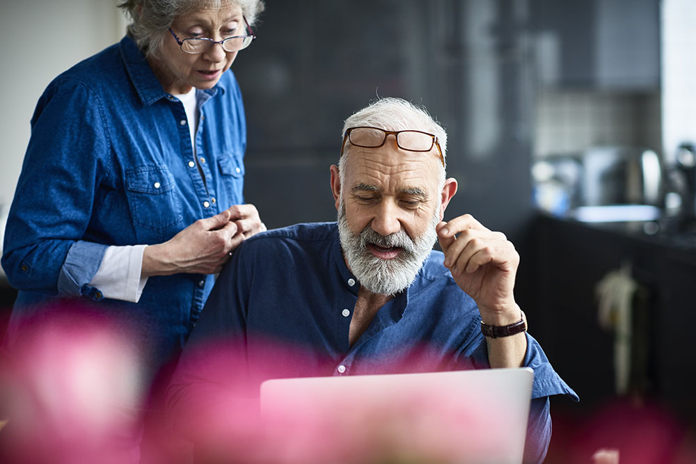 Two older people look at a computer.