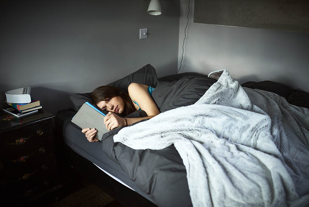 Woman uses a tablet in bed.