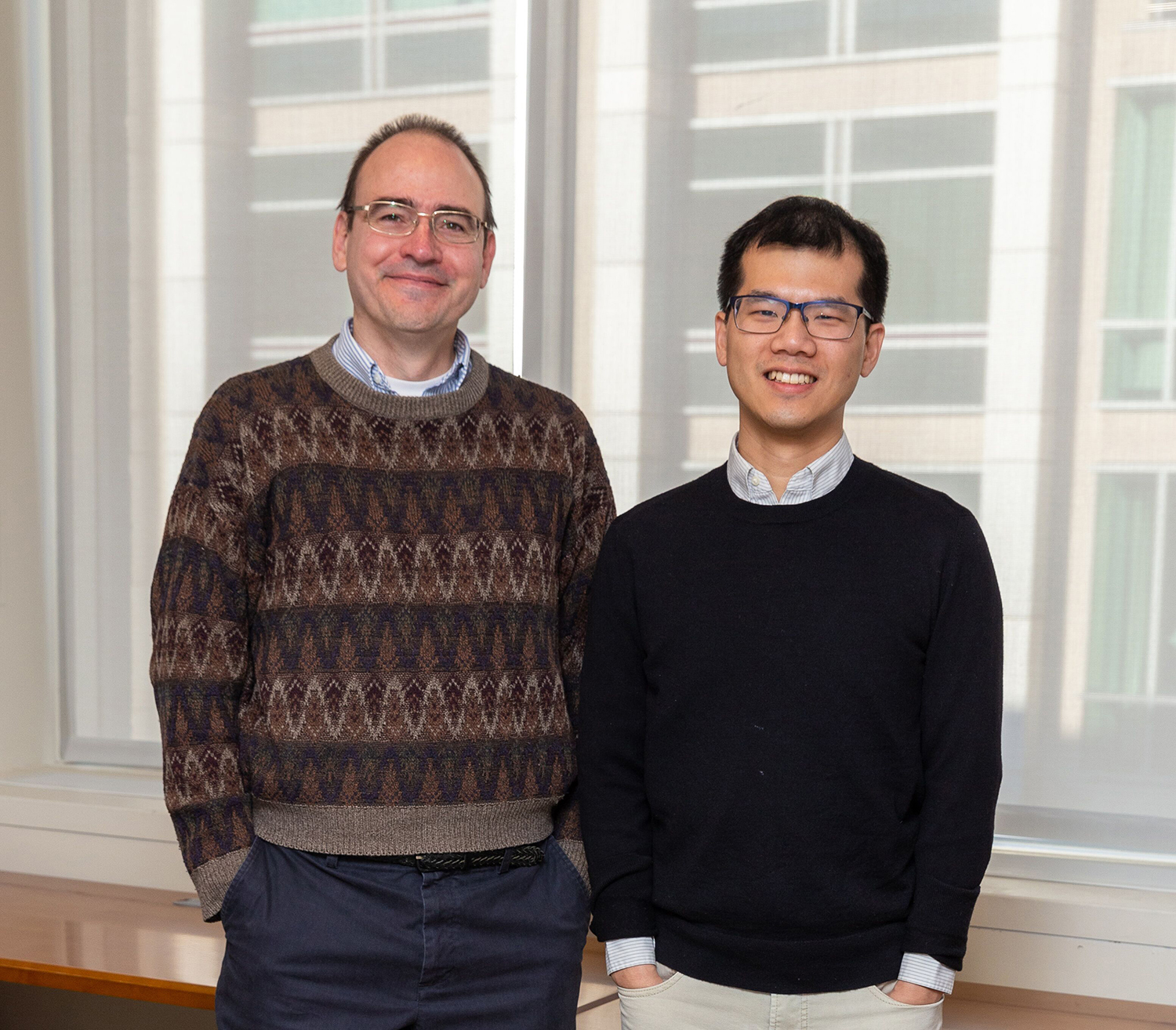 Two researchers pose in front of a window.
