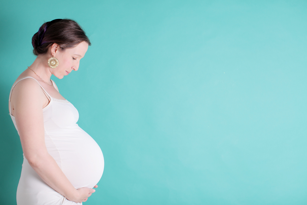 Profile of pregnant women holding her belly with a light blue background.