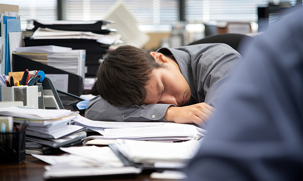 Exhausted office workers rests his head on top of documents covering his desk
