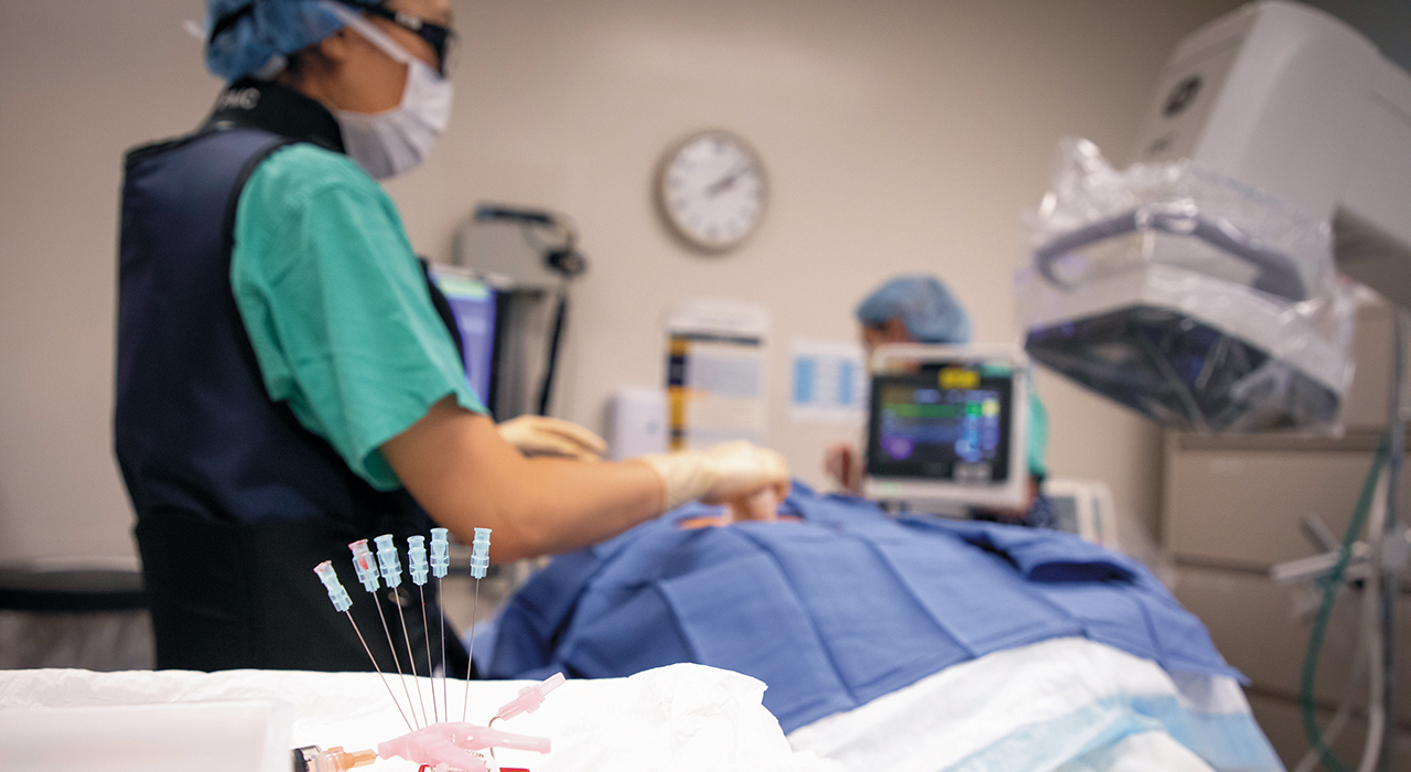 Needles in the foreground of various machines and a doctor in scrubs.