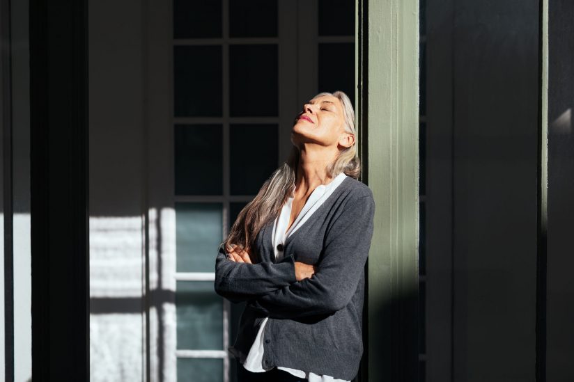 A woman leans on a post and basks in the sun.