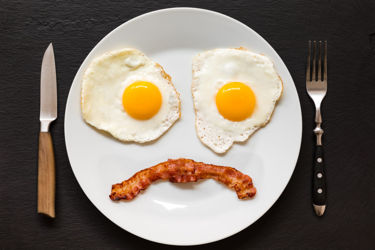 Eggs and bacon arranged into a sad face on a plate.