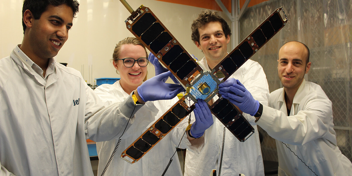 Researchers hold miniature satellite.
