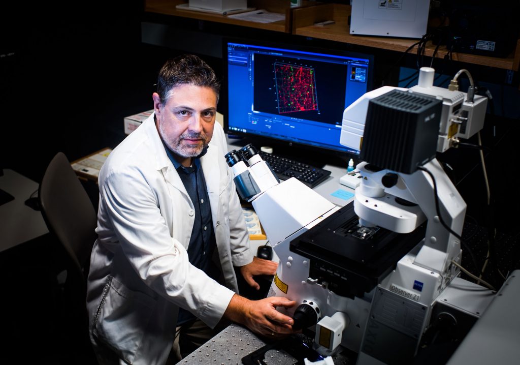 BU researcher Basilis Zikopoulos poses with a microscope.
