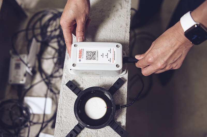 "‘Talking’ concrete could help prevent traffic jams and cut carbon emissions; From beneath a concrete pour, this black circular sensor transmits data about the concrete’s strength levels through a cord plugged into an above-ground handheld device called a data logger. Engineers receive real-time data from this device through a smartphone app. (Purdue University photo/Rebecca McElhoe)"