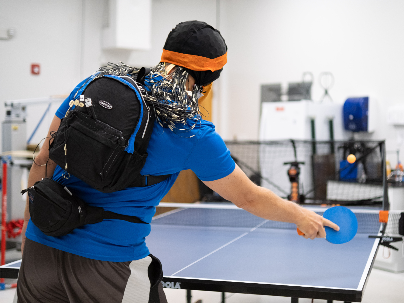 Playing Sports Against Robotic Opponents Makes Our Brains Work Harder, A research participant plays against a ball-serving machine while his brain is imaged with an EEG cap. Image by Frazier Springfield.