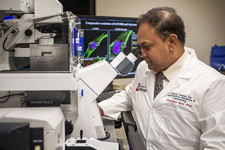 "Picture: Chandan K Sen, PhD looking through a microscope"