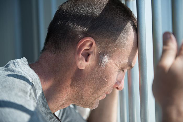 Image of man leaning on prison bars