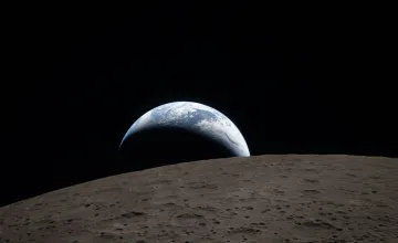 Earthset captured through the Orion spacecraft window during the Artemis II crew’s flyby of the Moon. A muted blue Earth with bright white clouds sets behind the cratered lunar surface. 