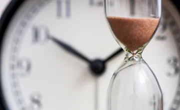 Hourglass in front of clock, depicting time passing. 