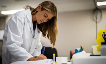 Researcher in a lab coat taking notes. 