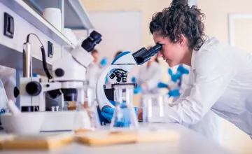 Researcher in lab observing looking into a microscope