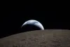 Earthset captured through the Orion spacecraft window during the Artemis II crew’s flyby of the Moon. A muted blue Earth with bright white clouds sets behind the cratered lunar surface. 