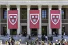 Students standing on stairs with red insignia banners overhead at Harvard University.