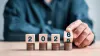 Wooden blocks reading 2025/6 sit atop stacks of coins