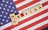Wooden blocks spell out H1B Visa against a U.S. flag.