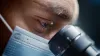 Scientist Wearing Surgical Mask and Looking into the Microscope